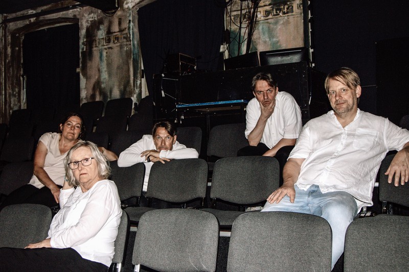 Hottenlotten sitzen im Theater auf Zuschauerstühlen und schauen den Betrachter nachdenklich an.  